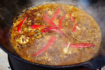 National Uzbek dish pilaf, pilaw, plov, rice with meat in big pan. Cooking process in a cauldron on fire. Preparation stage. pour out rice, Add waters, red pepper and the whole garlic