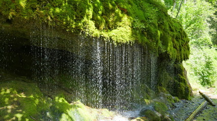 Wasserfall, Wassertropfen über einem moosbehangenem Felsen als Wasservorhang