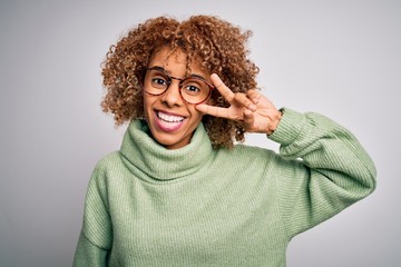 Young beautiful african american woman wearing turtleneck sweater and glasses Doing peace symbol with fingers over face, smiling cheerful showing victory