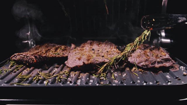 Delicious juicy meat steak cooking on grill. Kitchen tongs. Aged prime rare roast grilling tenderloin fresh marble tenderness beef. Prime beef fry on electric roaster, rosemary black pepper, salt.