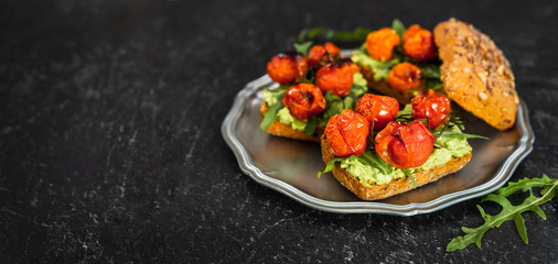 Fototapeta na wymiar Delicious vegan sandwiches with mashed avocado, roasted tomatoes and arugula