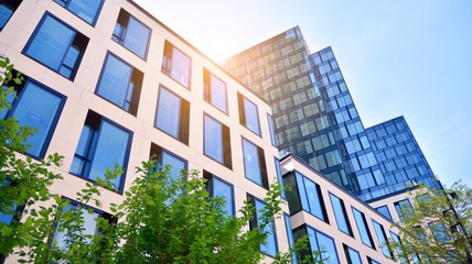 Bottom view of office building window close up with sunrise, reflection and perspective. Modern architecture with sun ray. Glass facade on a bright sunny day with sunbeams on the blue sky. 