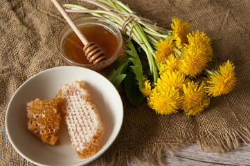 A bouquet of yellow dandelion flowers and a Cup with honey and honeycomb on a burlap on a wooden...