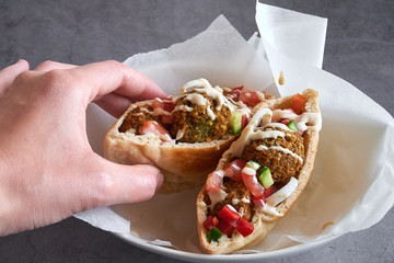 Woman hand hold an authentic fresh falafels balls inside of two halves of pita bread sandwich with...