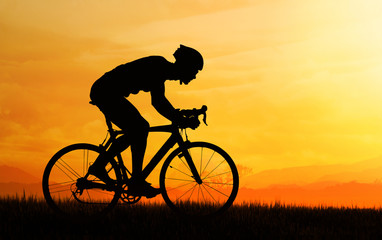 Obraz premium Silhouette of cyclist riding in the field and orange sunset sky.