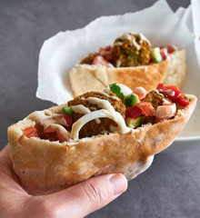 Woman hand hold an authentic fresh falafels balls inside of half pita bread sandwich with chopped salad and drizzle of tahini sauce on top, close-up of chickpea falafel in gluten-free pita