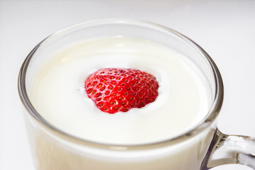 red fresh ripe sweet strawberries floating in cow's milk poured in a clear glass glass on a white background Breakfast place for text
