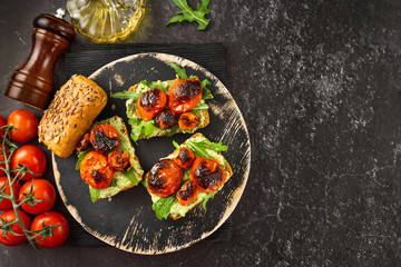 Flat lay of three vegan sandwiches on a wooden tray with avocado, tomatoes and arugula