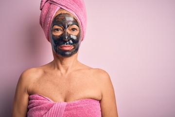 Middle age brunette woman wearing beauty black face mask over isolated pink background Relaxed with serious expression on face. Simple and natural looking at the camera.