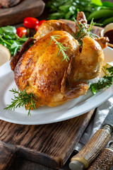 Whole Roasted Chicken on white plate with rosemary, sauces and vegetables