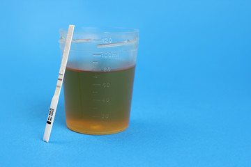 Positive ovulation test and a urine container. Copy space