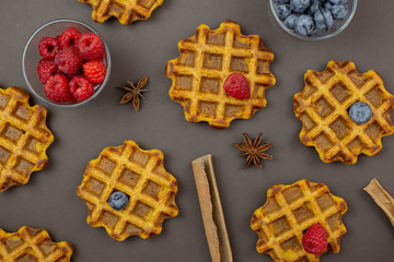 Belgian, carrot waffles with maple syrup and fresh raspberries, blueberry, cinnamon and star anise . Dark background. Top view. 