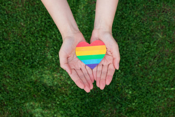 Womans hands hold heart in the colors of rainbow on grass background. LGBT rights, Pride month,...