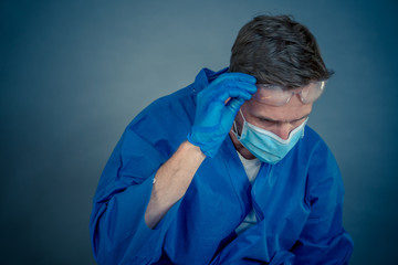 Male doctor feeling exhausted after long shift treating coronavirus infected patients at hospital