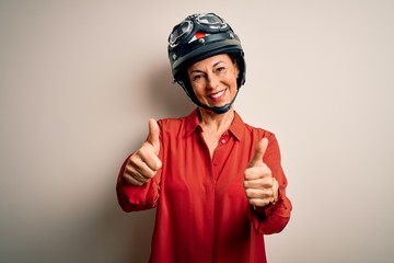 Middle age motorcyclist woman wearing motorcycle helmet over isolated white background approving doing positive gesture with hand, thumbs up smiling and happy for success. Winner gesture.