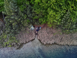 Aerial view of 2 people tent camp at green lake with bonfire at sunset.