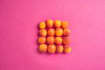 Fototapeta na wymiar Square of fresh apricots over pink background, top view