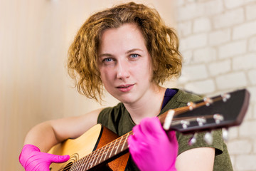 A young pretty teen girl stares at the camera and plays the guitar in rubber gloves, learning...