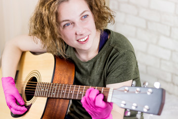A young teenage girl smiles and plays the guitar in rubber gloves and learns chords or a song....