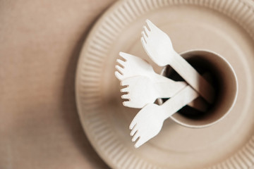 Wooden forks and paper cups with plates on kraft paper background. Eco friendly disposable tableware. Also used in fast food, restaurants, takeaways, picnics. Top view. Copy, empty space for text