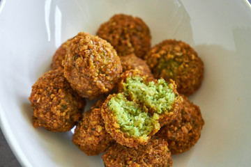 Close-up on woman hands hold a fresh and crispy falafel ball cut in half, authentic deep fried chickpea hot round falafels ball in the background