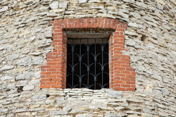 Fototapeta na wymiar Restored window with wrought-iron bars in the old watchtower of rough stone. Copy space.