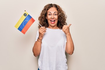 Middle age beautiful tourist woman holding venezuelan flag over isolated white background pointing thumb up to the side smiling happy with open mouth