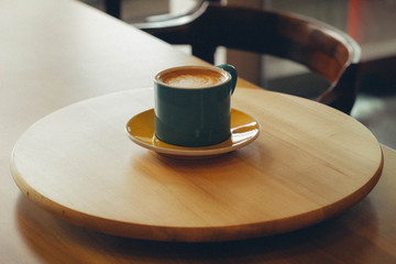 A gc of hot cappuccino on a wooden table in the morning.