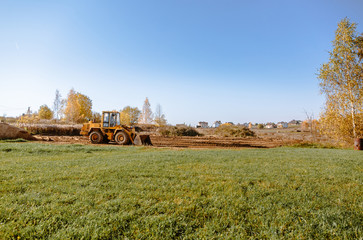 Fototapeta premium large yellow wheel loader aligns a piece of land for a new building. Preparation of the land for the auction. Leveling the landscape and adding sand for construction.