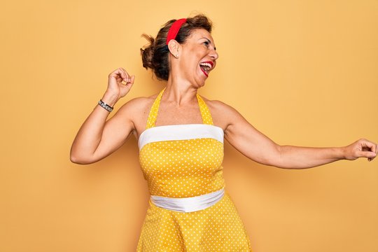 Middle Age Senior Pin Up Woman Wearing 50s Style Retro Dress Over Yellow Background Dancing Happy And Cheerful, Smiling Moving Casual And Confident Listening To Music