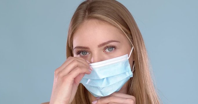 Young woman adjusting her medical face mask. Looking at camera with smile behind