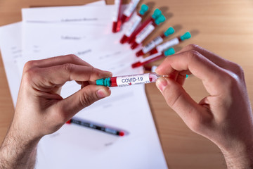 Medical test tube with blood test for coronavirus COVID-19 in men's hands, test results and test tubes with blood in the background