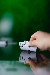 Hand showing two poker cards on the table with reflection on green background