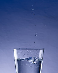 Detail of drops falling into glass of water with blue background-