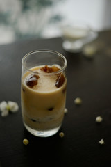 Ice coffee in glass on the dark wooden table with leafs behind