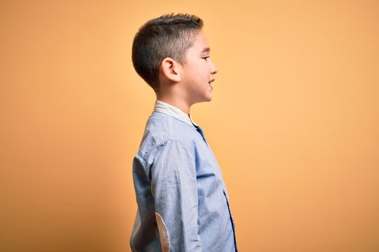 Young little boy kid wearing elegant shirt standing over yellow isolated background looking to side, relax profile pose with natural face with confident smile.