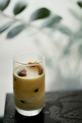 Ice coffee in glass on the dark wooden table with leafs behind
