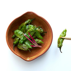 wooden Bowl with sweet green pepper pan fried and chopstick holding a green capsicum pepper, Sauted Shishito Peppers, from above, isolated
