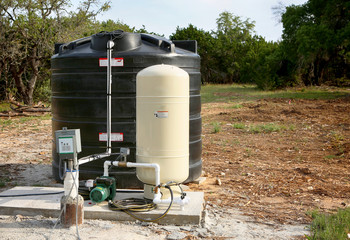 Deep water well set up, country side construction. Drilled draw well with pressure switch and storage tank.