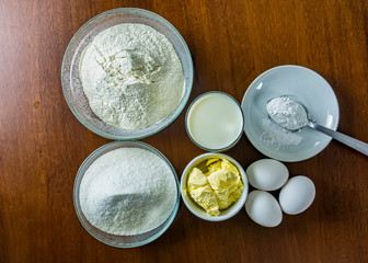 Basic ingredients for making cake, flour, sugar, milk, eggs, butter and yeast on wooden table. Ingredients for homemade cake