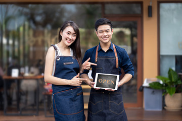 Two asian small business owners hands holding and showing with Open sign board in front of coffee shop.