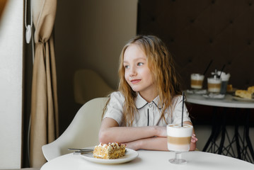 A cute little girl is sitting in a cafe and looking at a cake and cocoa close-up. Diet and proper nutrition