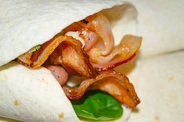 Leafy salad, sliced vegetables, sauce and fried bacon slices wrapped in pita bread. Delicious homemade Shawarma. Close up.
