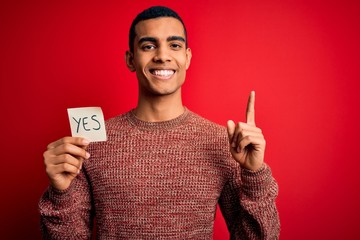 Young handsome african american man holding reminder paper with yes message surprised with an idea...