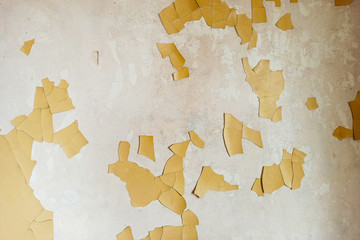 Old white plastered wall with partially peeling and cracked yellow paint.