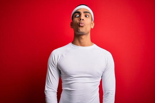 Young handsome african american sportsman wearing sportswear over red background making fish face with lips, crazy and comical gesture. Funny expression.