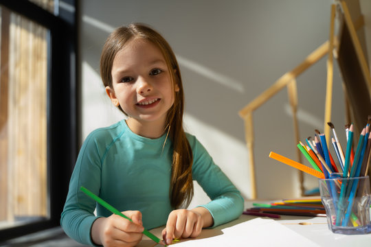 Cheerful little girl drawing with colored pencil at home