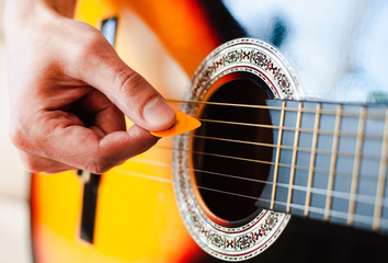 Male fingers with mediator playing on guitar strings. Close-up.