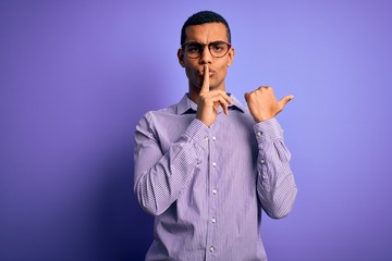 Handsome african american man wearing striped shirt and glasses over purple background asking to be quiet with finger on lips pointing with hand to the side. Silence and secret concept.