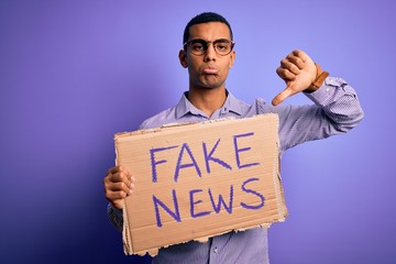 Young handsome african american man protesting holding banner with fake news message with angry face, negative sign showing dislike with thumbs down, rejection concept